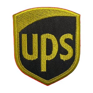 May include: Embroidered patch featuring the UPS logo. The patch has a shield shape with a gold border and a black and gold design. The letters "UPS" are in gold.