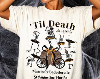 May include: An ivory t-shirt featuring a graphic of skeletons in tutus dancing around a leopard print carriage. The text reads 'Til Death do us party', 'EST. 2026', 'Martina's Bachelorette', and 'St Augustine Florida' in black and orange lettering.