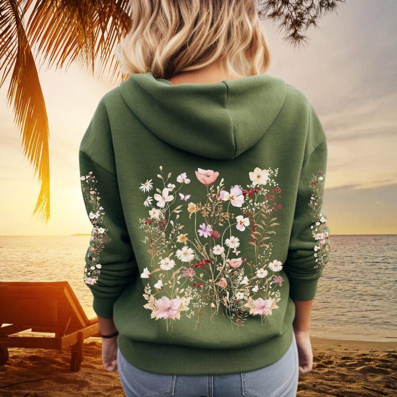 Pu&ograve; includere: Una felpa con cappuccio verde con una stampa floreale sul retro. La stampa presenta una variet&agrave; di fiori in tonalit&agrave; di rosa, bianco e giallo.