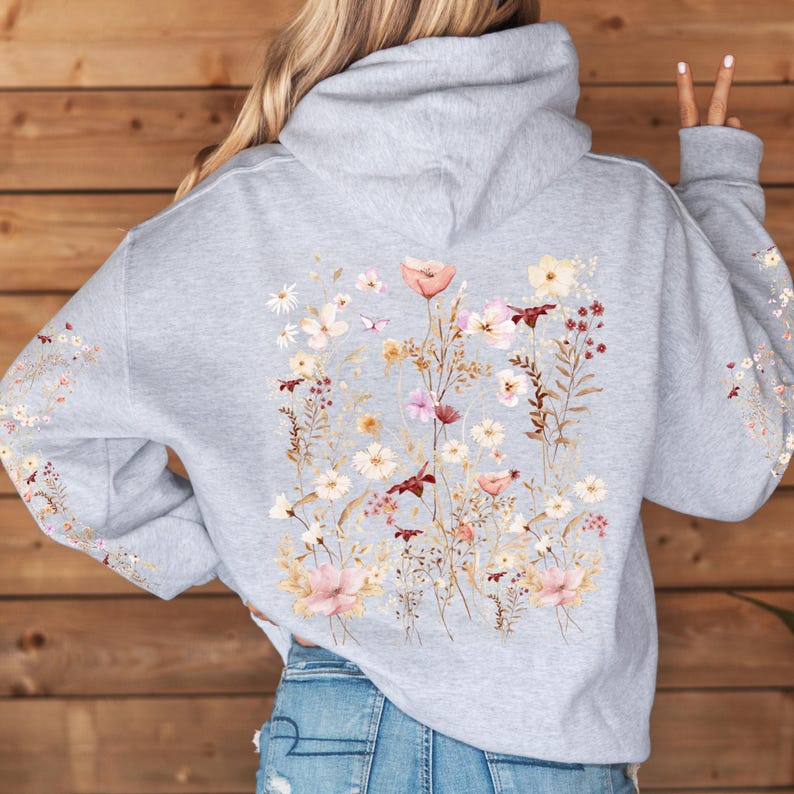 Pu&ograve; includere: Una felpa con cappuccio grigia con una stampa floreale sul retro. La stampa presenta una variet&agrave; di fiori in tonalit&agrave; di rosa, bianco e marrone.