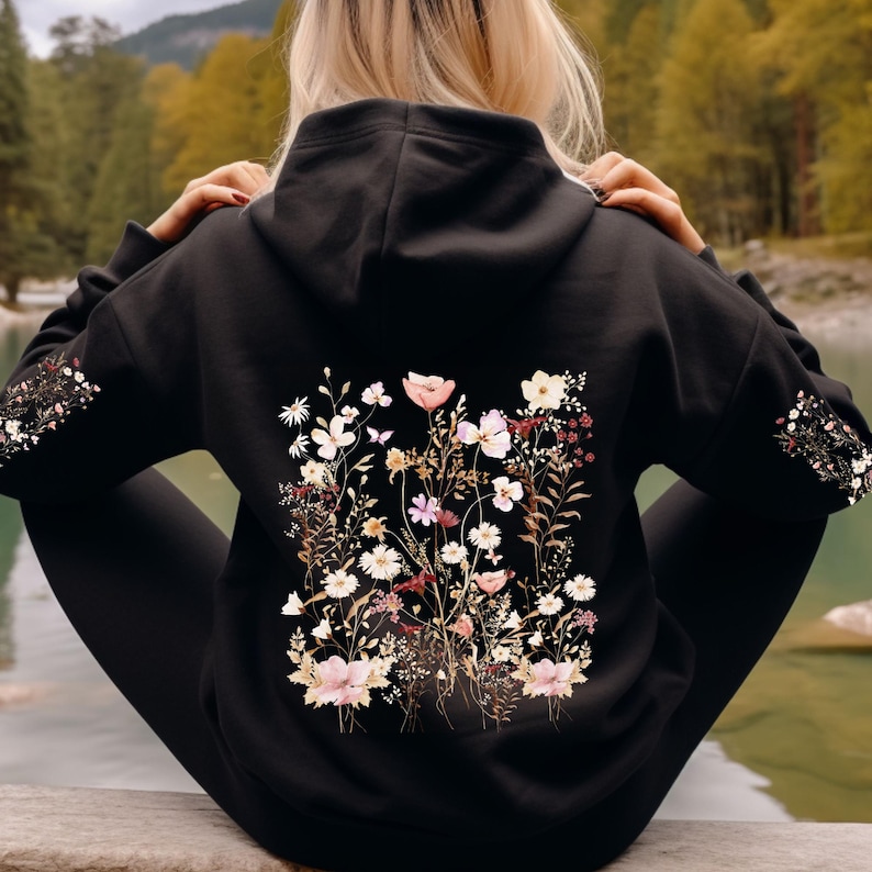 Pu&ograve; includere: Felpa con cappuccio nera con una stampa floreale sul retro. La stampa presenta una variet&agrave; di fiori in tonalit&agrave; rosa, bianco e marrone.