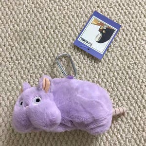 May include: A plush purple mouse-like creature with soft fur, small ears, and a silver carabiner attached to the top. A rectangular purple tag is attached, featuring an illustration of a character and the Japanese text 千と千尋の神隠し.