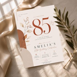 May include: A rectangular birthday invitation card featuring the text Celebrating 85 Years of A Life of Wisdom, Love & Beautiful Memories, Amelia's 85th Birthday Celebration, The Ivy Lounge, 123 Collins Street, Melbourne VIC 3000, 21 March 2026.
