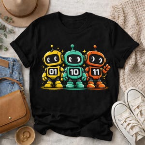 Puede incluir: Camiseta negra con tres robots de dibujos animados coloridos. Los robots amarillos, turquesa y naranja muestran los números 01, 10 y 11. Los robots tienen cabezas redondas, ojos grandes y están rodeados de estrellas amarillas.