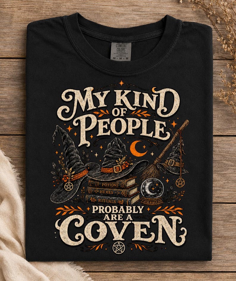 May include: A black t-shirt featuring a graphic print with the text "MY KIND OF PEOPLE PROBABLY ARE A COVEN". The design includes three witch hats, a stack of books labeled "POTIONS", "HEXES", and "RITUALS", a broom, a crystal ball, and a crescent moon.
