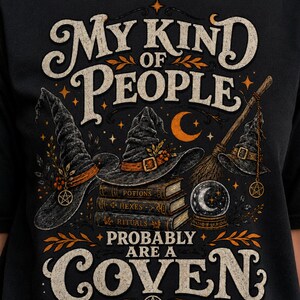 May include: A black t-shirt featuring a graphic print with the text "MY KIND OF PEOPLE PROBABLY ARE A COVEN". The design includes three witch hats, a stack of books labeled "POTIONS", "HEXES", and "RITUALS", a broomstick, and a crystal ball.