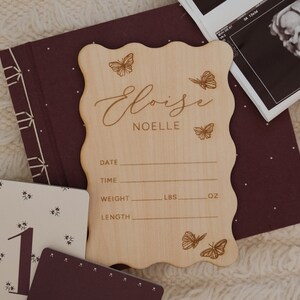 May include: A wooden birth announcement sign with the name "Eloise Noelle" and butterfly designs. The sign includes spaces for date, time, weight (lbs, oz), and length. Also shown are sonogram images and milestone cards.
