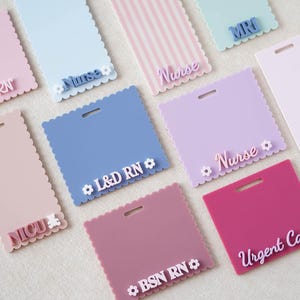 May include: A collection of rectangular and square acrylic badge reels with scalloped edges in various pastel and solid colors. Each piece features a horizontal slot at the top and raised lettering displaying titles like Nurse, L&D RN, NICU, MRI, BSN RN, and Urgent Care.