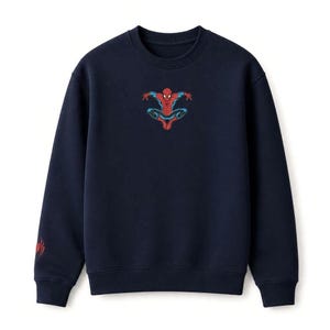 May include: Navy blue sweatshirt featuring a Spider-Man graphic in red, blue, and black. The superhero is depicted in a dynamic pose. A smaller Spider-Man logo is on the left sleeve. This sweatshirt is perfect for fans of the Marvel comic book character.