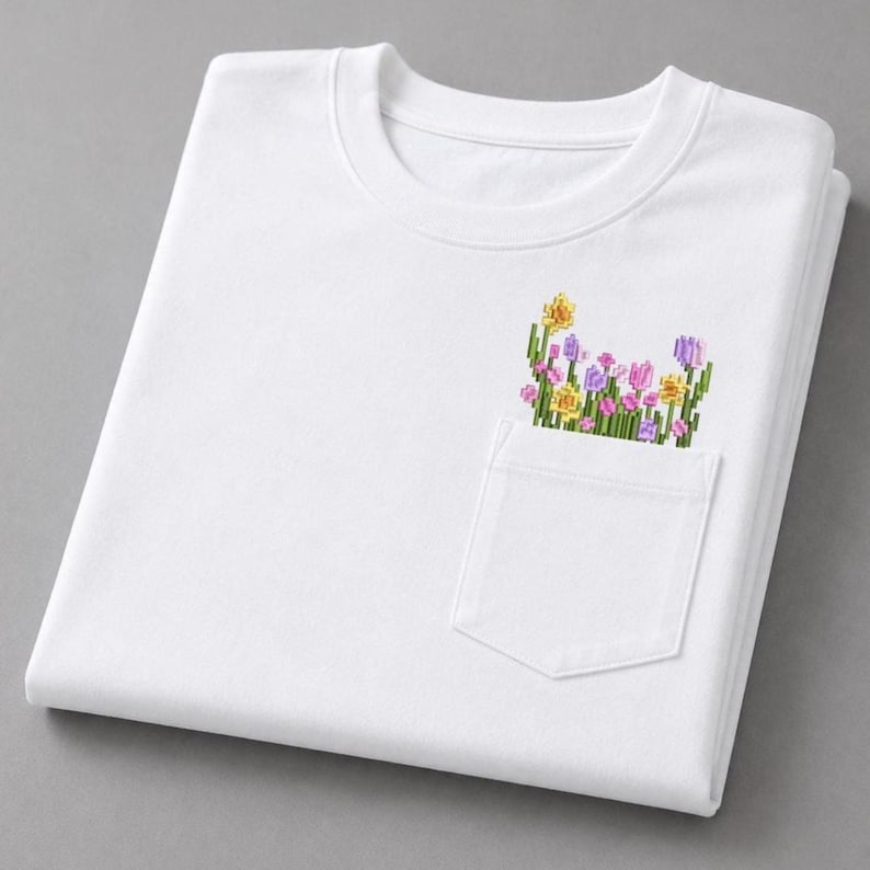 K&ouml;nnte beinhalten: Wei&szlig;es Sweatshirt mit Rundhalsausschnitt und einer Tasche mit farbenfroher Blumenstickerei. Die Stickerei umfasst gelbe, rosa und lila Blumen mit gr&uuml;nen Stielen. Das Sweatshirt ist sauber auf einer grauen Oberfl&auml;che gefaltet.