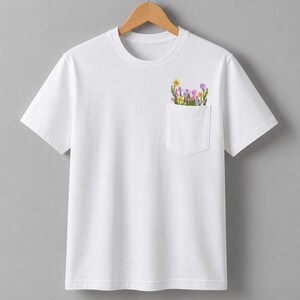 K&ouml;nnte beinhalten: Wei&szlig;es T-Shirt mit einer Tasche mit einem bunten Blumenmuster. Die Tasche ist mit gelben, lila und rosa Blumen gef&uuml;llt. Das Shirt hat einen klassischen Rundhalsausschnitt und kurze &Auml;rmel.