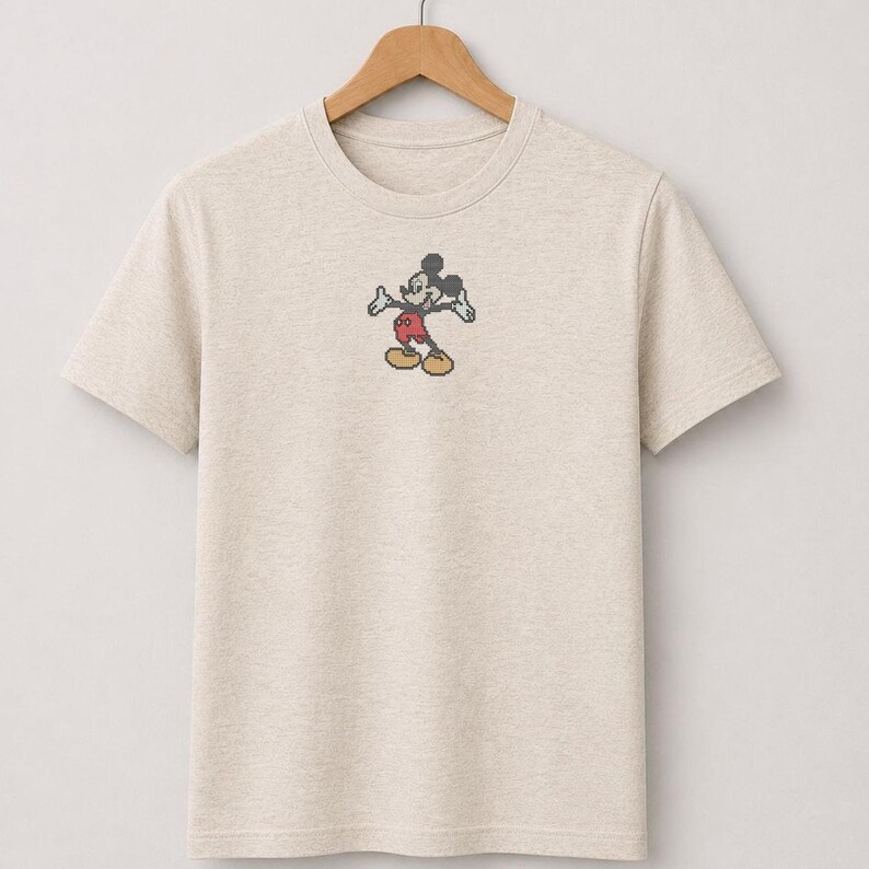 Pu&ograve; includere: Una t-shirt a maniche corte color beige m&eacute;lange con una piccola grafica pixelata di Mickey Mouse centrata sul petto. Il personaggio &egrave; raffigurato in una posa classica con orecchie nere, pantaloncini rossi e scarpe gialle in stile griglia.