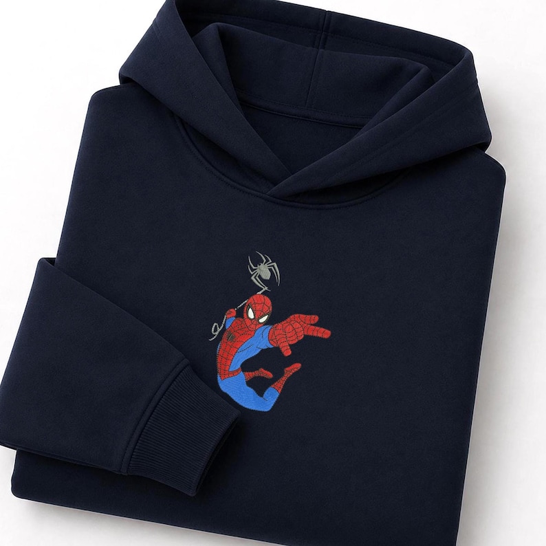 May include: A dark navy blue hooded sweatshirt featuring an embroidered graphic of a red and blue superhero character in a dynamic pose with a spider positioned above the character's head. The hoodie has long sleeves with ribbed cuffs.