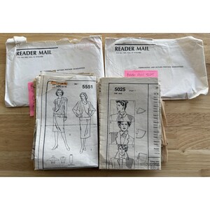 May include: A collection of vintage sewing patterns, featuring illustrations of women's clothing designs. The patterns are accompanied by white envelopes labeled "READER MAIL". The patterns include designs for dresses, tops, and jackets. The patterns are on a light brown wooden surface.