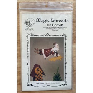May include: A clear plastic package containing a cloth doll pattern. The pattern is titled "Magic Threads On Comet!" and features a Santa Claus doll design with a star and a birdhouse. The pattern is 50.8 cm in size.