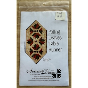 Könnte beinhalten: Ein Quiltmuster-Paket für einen "Falling Leaves Table Runner". Das Design zeigt ein geometrisches Muster aus roten und grünen Blättern auf beigem Hintergrund. Fertige Größe: 48 cm x 107 cm. Die Verpackung befindet sich in einer transparenten Plastikhülle.
