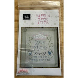 May include: A cross-stitch kit in a clear plastic bag. The kit features a design with the words "Happily Ever After" and the name "Zoe Marie" with the date "10.7.09". The design includes a crown and two blue birds.