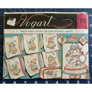 May include: A Vogart transfer pattern envelope, number 672, titled Dutch Treat Motifs for Your Kitchen & Dinette. The packaging features illustrations of children in traditional clothing, each labelled with a day of the week, plus kitchen-themed designs.