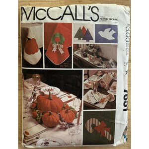 May include: A vintage McCall's pattern envelope featuring various holiday-themed sewing projects. The cover showcases images of table settings, including pumpkins, wreaths, and gingerbread houses. The text "MCCALL'S" is prominently displayed.