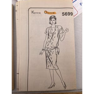 May include: Vintage sewing pattern featuring a flapper-style dress design. The illustration shows a woman in a knee-length dress with a tied waist and short sleeves. The pattern number is 5699, with size options K (8-10-12) and O (12-14-16).