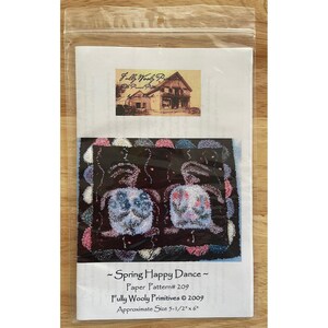 May include: A paper pattern titled "Spring Happy Dance" featuring a folk art design of two figures with blue and pink accents on a black background. The pattern is from Fully Wooly Primitives and measures approximately 5.5" x 6".
