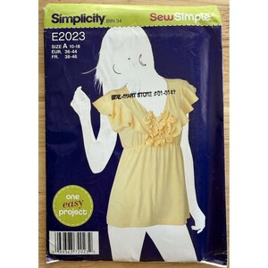 May include: A Simplicity sewing pattern, E2023, showing a yellow top with ruffles and floral details. The pattern includes sizes A 10-18, EUR 36-44, and FR 38-46. The text "WAL-MART STORE #01-0141" is visible. The pattern is labeled as "one easy project."