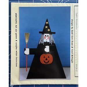 May include: A Halloween-themed yard ornament pattern featuring a witch design. The witch wears a black hat with gold stars, a black cloak, and holds a broom and a jack-o'-lantern. The pattern includes full-size instructions. The text reads "Yard Ornaments" and "Designs by Sandi Gore Evans & Carol McNaught."