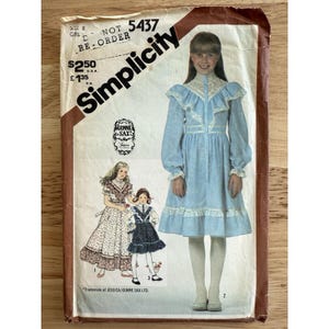 Könnte beinhalten: Vintage Simplicity Schnittmuster für ein Mädchenkleid. Die Schnittmusterhülle zeigt Illustrationen der Kleiderdesigns, darunter ein hellblaues Kleid mit Spitzenbesatz. Der Text auf der Hülle enthält "Simplicity" und "GUNNE SAX".