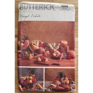Pode incluir: Um padrão de costura Butterick vintage com uma ilustração de natureza morta de frutas e vegetais. A capa mostra cestas de produtos, incluindo maçãs, peras e cenouras. O texto "Butterick" e "Margit Echols" são visíveis.