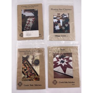May include: Four packaged quilt patterns. The patterns are in clear plastic bags with brown paper backing. The patterns include: Cookie Cut Starburst, Floating Star Charmer, Charming Funky Four Patch, and Stars.