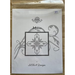 May include: A white paper package featuring the word "Mihrab" in a stylized font, with an ornate cross-shaped design in a black square. The package also includes the text "By SEBA Designs".