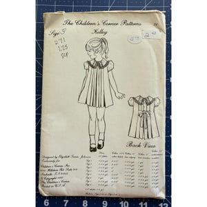 Könnte beinhalten: Vintage Schnittmuster mit dem Titel "The Children's Corner Patterns Kelley". Das Muster zeigt eine Strichzeichnung eines Mädchens in einem Kleid mit einem Bubikragen. Enthält eine Rückansicht-Illustration und Stoffanforderungen. Gedruckt in den USA.