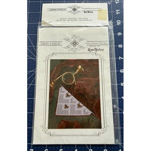 May include: A sealed Cross 'N Patch needlepoint kit package. The front image displays a partially finished needlepoint project, a gold-coloured magnifying glass, and other decorative items. The package features the text "Cross 'N Patch" and "Emie Bishop".