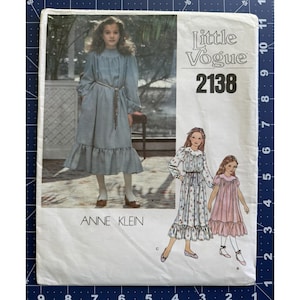 Puede incluir: Un sobre de patrón de costura Little Vogue 2138 de Anne Klein que presenta una fotografía de un vestido de manga larga hasta la pantorrilla con un dobladillo con volantes y un cinturón fino, junto a ilustraciones de dos variantes del vestido.