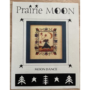 Pode incluir: Um padrão de ponto cruz intitulado "Prairie Moon" com um design emoldurado com uma figura, lua e estrelas. O design é cercado por motivos florais e de folhas. O texto "Moon Dance" está abaixo da imagem emoldurada, com gráficos de estrelas e árvores.