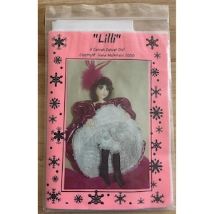 May include: A pink package featuring a doll dressed as a cancan dancer. The doll has a burgundy dress, white ruffled skirt, and a feathered hat. The package has snowflake and star designs and the text "Lilli". Copyright Diane McDonald 2000.