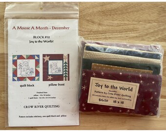 Könnte beinhalten: Eine transparente Plastiktüte mit einem Quiltmuster und einem Stoffbündel. Das Muster trägt den Titel "A Moose A Month - December" mit dem Text "Joy to the World!". Das Stoffbündel misst 45,7 x 45,7 cm.