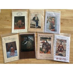 May include: A collection of sewing patterns in plastic sleeves, featuring various Halloween-themed designs. The patterns include scarecrows, witches, and other festive characters. The text on the patterns includes "Hank, the Scarecrow" and "Sew Many Prims."