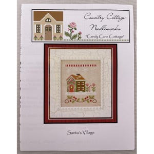 Può includere: Un modello a punto croce per "Candy Cane Cottage" di Country Cottage Needleworks. Il design presenta un cottage festivo con una porta a bastoncino di zucchero, circondato da fiori e fiocchi di neve, incorniciato in un bordo rosso. Il testo "Santa's Village" è in basso.