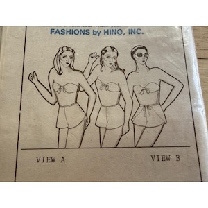 May include: A vintage sewing pattern envelope from FASHIONS by HINO, INC. featuring a black and white line drawing of three figures wearing two-piece swimwear sets with tie-front tops and shorts, labeled as VIEW A and VIEW B on the paper.