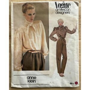 以下が含まれることがあります： ヴィンテージVogue American Designersの裁縫パターン、アン・クラインのデザイン。パターンには、ネクタイ付きのブラウスとハイウエストパンツのイラストが含まれています。表紙はベージュと茶色の配色です。