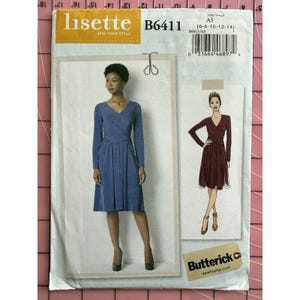 Könnte beinhalten: Ein Schnittmuster von Lisette, B6411, mit einem Wickelkleid-Design. Das Muster zeigt das Kleid in Blau und Burgunderrot. Die Mustergröße ist A5, passend für die Größen 6-8-10-12-14. Das Muster befindet sich auf einem rosa-weißen Gitterhintergrund.