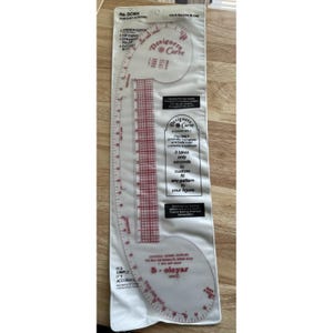 May include: A clear plastic Designers Curve ruler set in a white plastic sleeve. The set includes a French curve, hip curve, straight ruler, and cutout block. The text on the sleeve reads "For Easy Altering" and "The ONLY accurate, complete armhole ruler available anywhere."