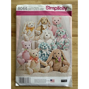 Puede incluir: Patrón de costura Simplicity 8044 con varios diseños de animales de peluche, incluyendo osos y conejos. El patrón incluye múltiples tallas y está impreso en los EE. UU. Los animales son de varios colores y patrones, con lazos y otros elementos decorativos.
