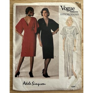 Peut inclure: Une pochette de patron de couture Vogue Patterns American Designer pour le modèle Adele Simpson 1254. Le recto présente deux modèles portant des robes mi-longues à encolure en V et manches larges, ainsi qu'un croquis de robe longue fendue.