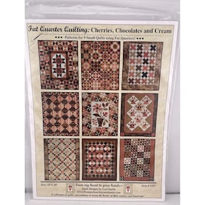 Pode incluir: Um padrão de colcha intitulado "Fat Quarter Quilting: Cherries, Chocolates and Cream". O padrão apresenta nove pequenos desenhos de colchas em tons de castanho, creme e vermelho. A embalagem tem 40,6 cm x 50,8 cm e inclui o texto "From my heart to your hands."