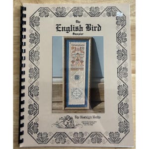 May include: A spiral-bound instructional booklet titled The English Bird Sampler with a black and white floral border. The cover features a photograph of a framed vertical needlework sampler with birds, alphabet letters, and geometric patterns.