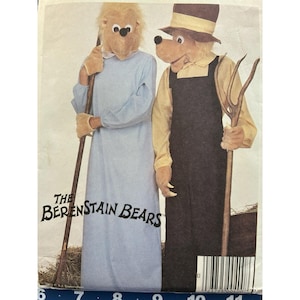 May include: A sewing pattern envelope for The Berenstain Bears costumes. One figure wears a light blue long-sleeved gown with tan gloves and holds a rake. The other wears a yellow checkered shirt, black overalls, and a brown hat, holding a pitchfork.
