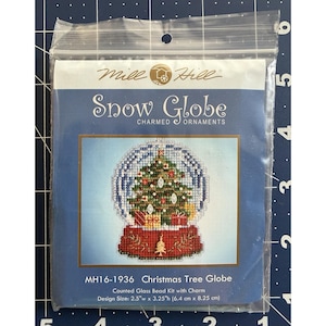 May include: A Mill Hill Snow Globe Charmed Ornaments counted glass bead kit with charm, model MH16-1936 Christmas Tree Globe. The package displays a cross-stitch design of a snow globe containing a Christmas tree and gifts, measuring 2.5"w x 3.25"h.