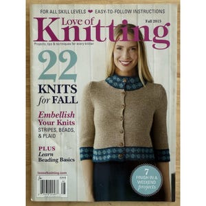 以下が含まれることがあります： 「Love of Knitting」という雑誌の表紙で、女性が青いトリムが付いたベージュのカーディガンを着ています。表紙には「22 Knits for Fall」、「Embellish Your Knits」、「Learn Beading Basics」と書かれています。雑誌は2015年秋号です。